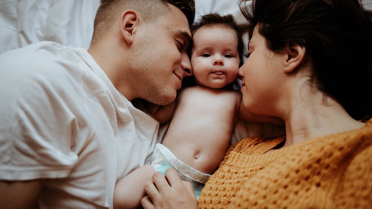 A family enjoys a warm, intimate moment lying on the bed with their baby.